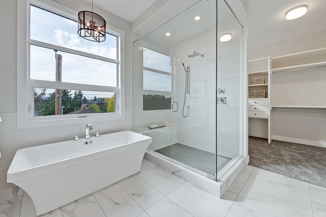 Modern bathroom with a freestanding bathtub, glass-enclosed shower, large window with city view, and walk-in closet with storage shelves.