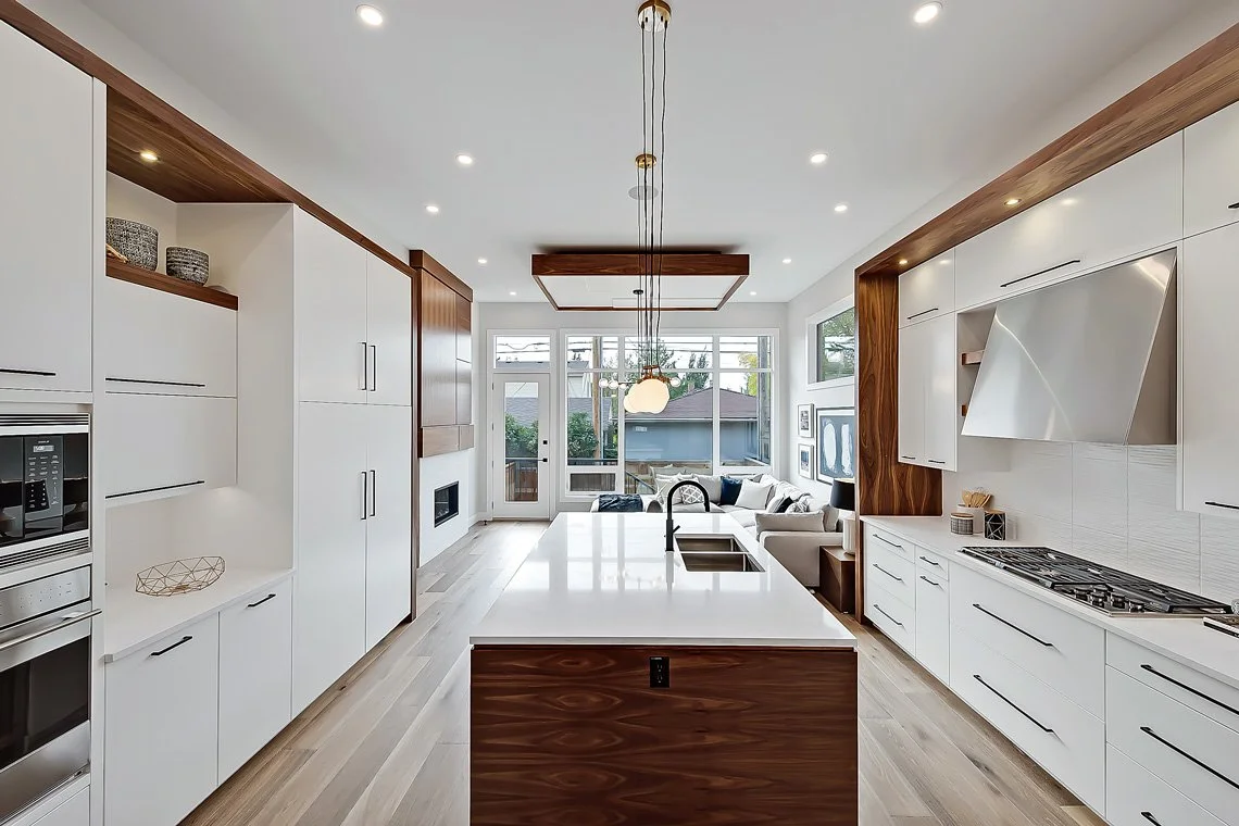 Modern kitchen with white cabinetry, a central island with a wooden base, and a living room with a sectional sofa visible in the background.