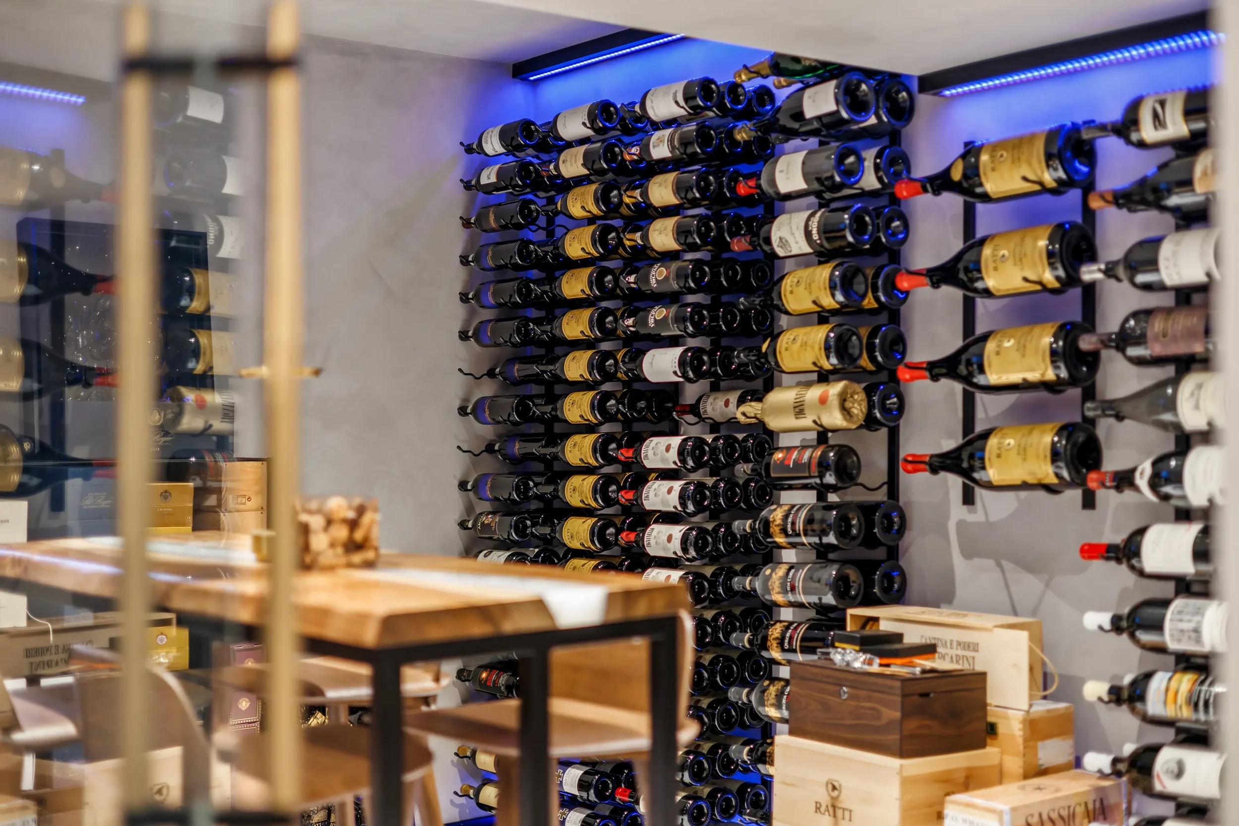 A wine cellar with shelves of wine bottles illuminated by blue lighting, with some wine boxes on the floor.