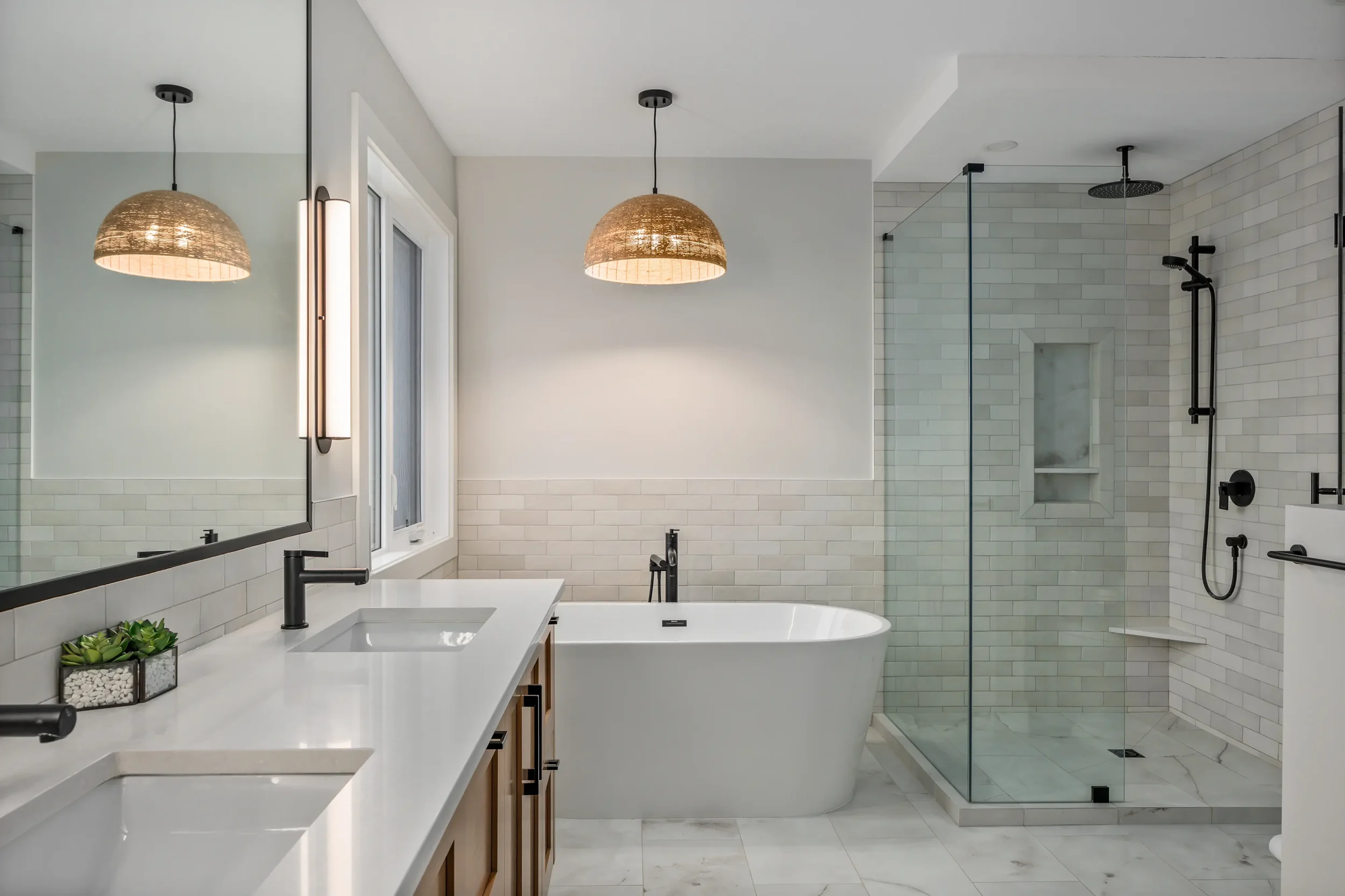 Modern bathroom with white subway tile walls, a freestanding bathtub, a double vanity with black fixtures, and a glass shower enclosure with black fixtures.