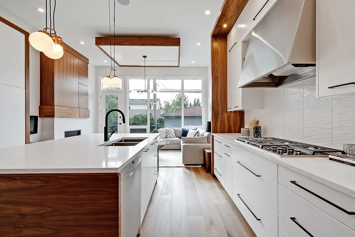 Modern kitchen with white cabinets, wooden accents, island with black sink, and view of living area with sitting area and large windows.