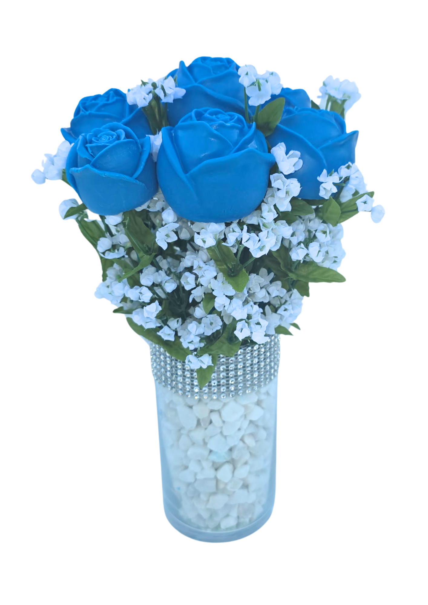 A bouquet of blue roses and white small flowers in a tall, clear glass vase decorated with rhinestones, filled with white stones.