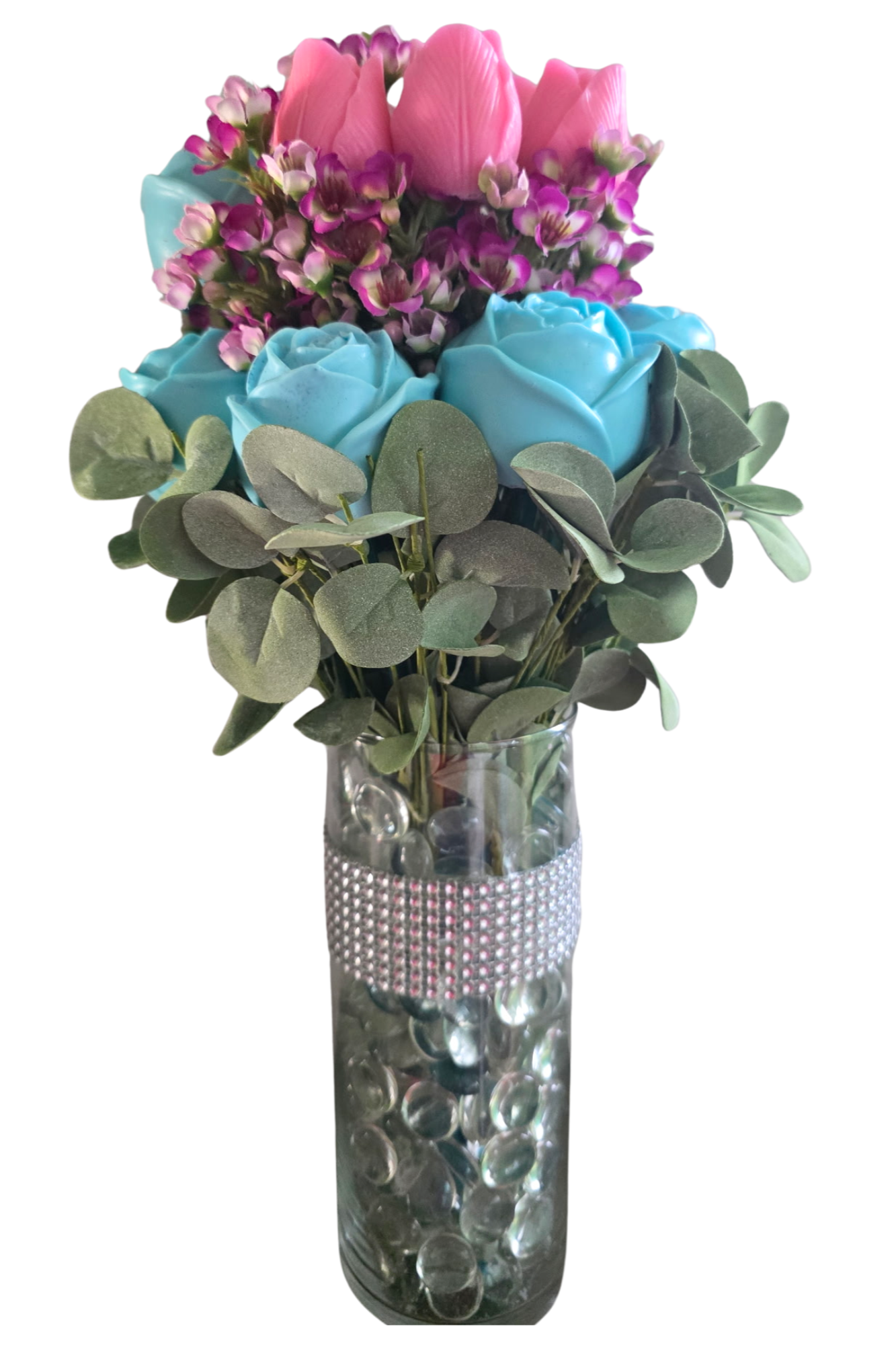 A clear glass vase with decorative rhinestones, containing pink tulips, blue roses, purple and white small flowers, and green eucalyptus leaves.
