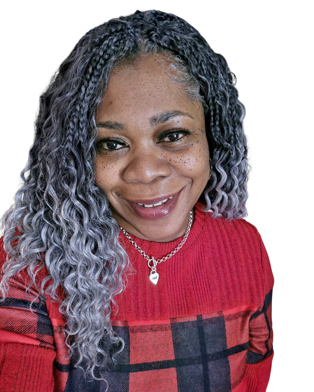 A woman with curly, gray-tipped hair, smiling, wearing a red sweater with a black plaid pattern and a silver necklace with a heart pendant.