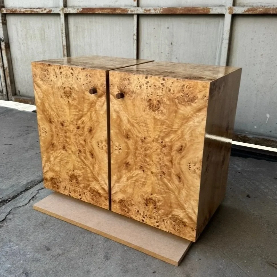 Wooden cabinet with burled wood grain pattern, placed on a cardboard base outside near a metal fence.