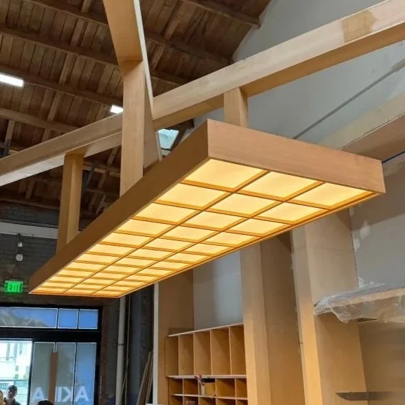 Large rectangular wood and frosted glass ceiling light fixture hanging from a wooden ceiling in a modern interior space.