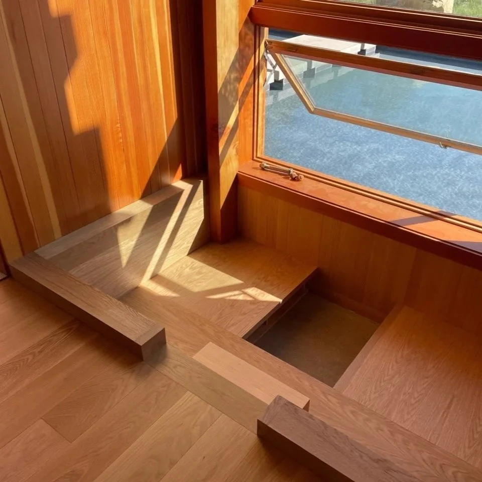 Sunlight illuminating a wooden stairway with a large open window showing an outdoor scene
