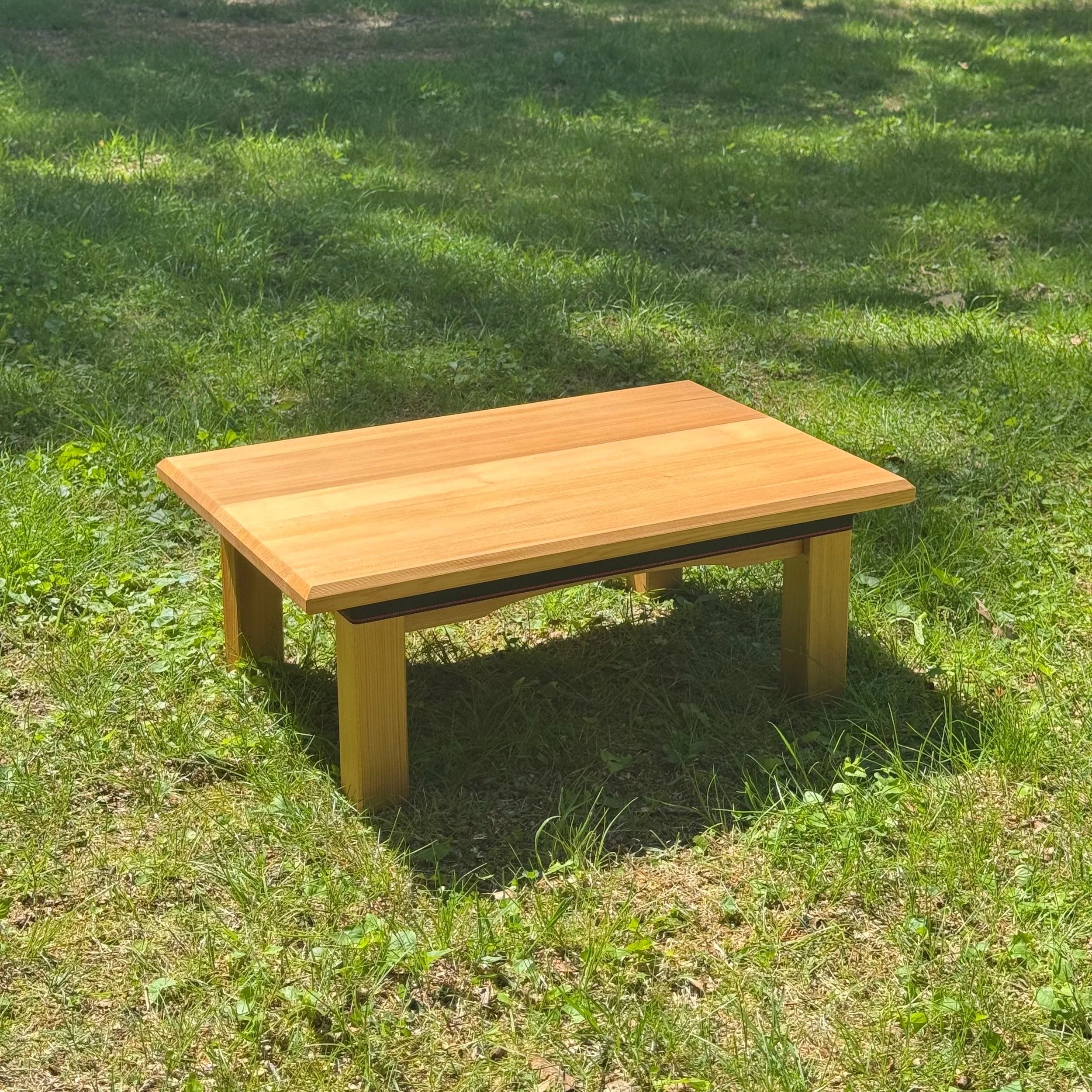 A wooden table outdoors on a grassy area, with sunlight and shade visible on the grass.
