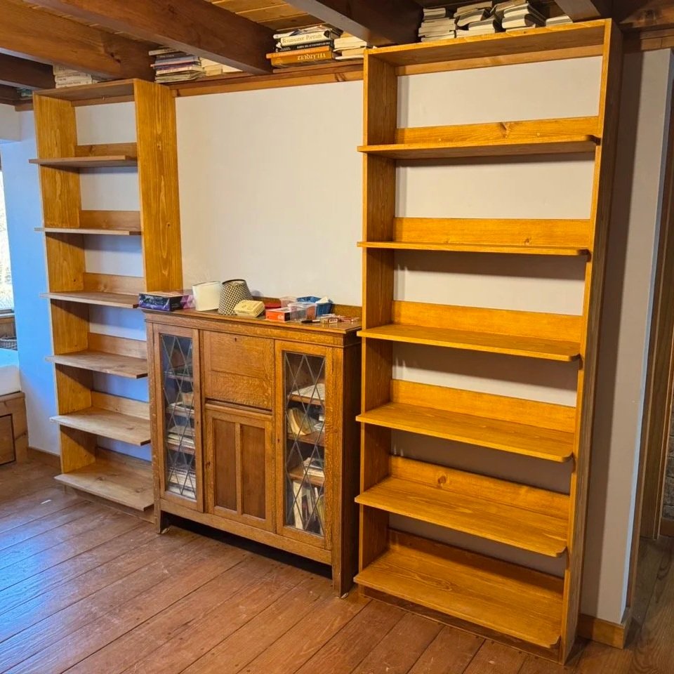 Two wooden bookshelves and a wooden cabinet with glass-paneled doors in a room with wood flooring and a wooden ceiling.