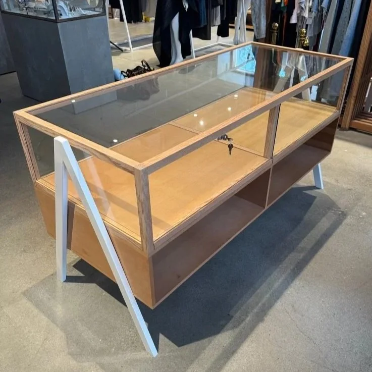 Wood display case with glass top and sliding glass doors, situated on a retail store floor with clothing racks in the background.
