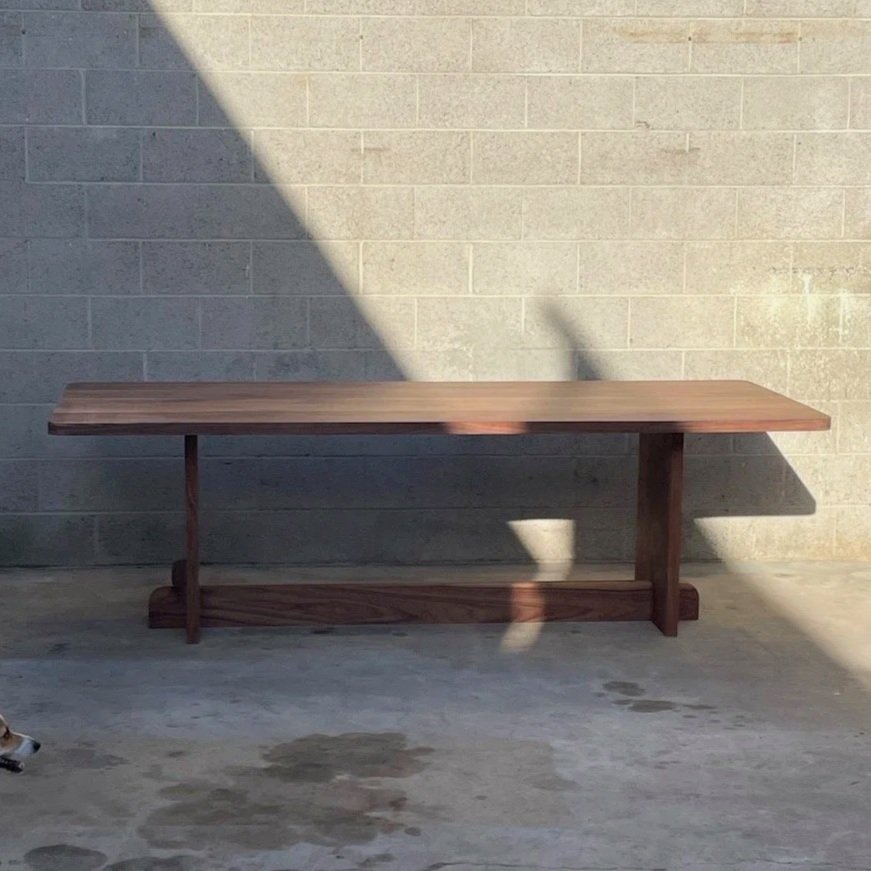 Wooden table against a concrete wall with a shadow cast on it, and a small dog visible at the lower left corner.