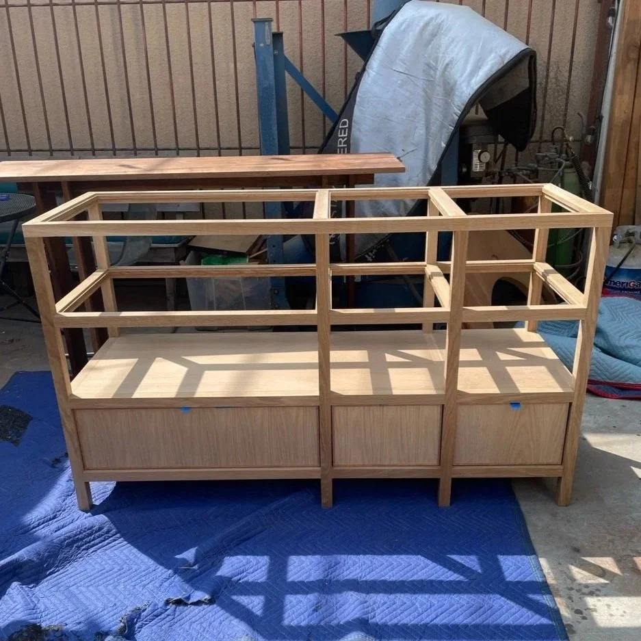 Wooden frame structure being built, placed on a blue quilted blanket outside, with tools and materials around.