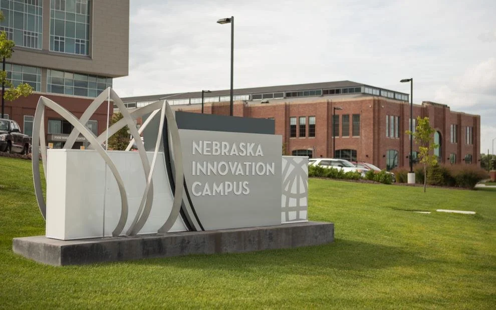 Sign that reads 'Nebraska Innovation Campus' in front of a modern brick building on a grassy area.