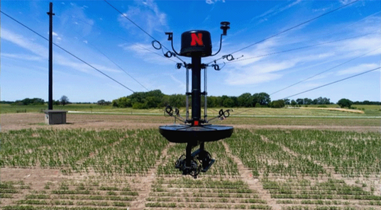 A weather balloon with the Nebraska logo floating above a farm field with crops.