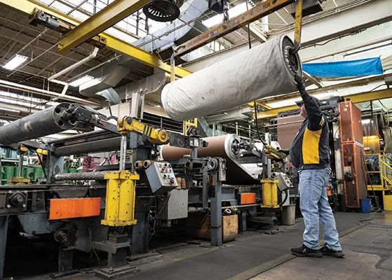 Worker in a manufacturing plant operating machinery with large rolls of material