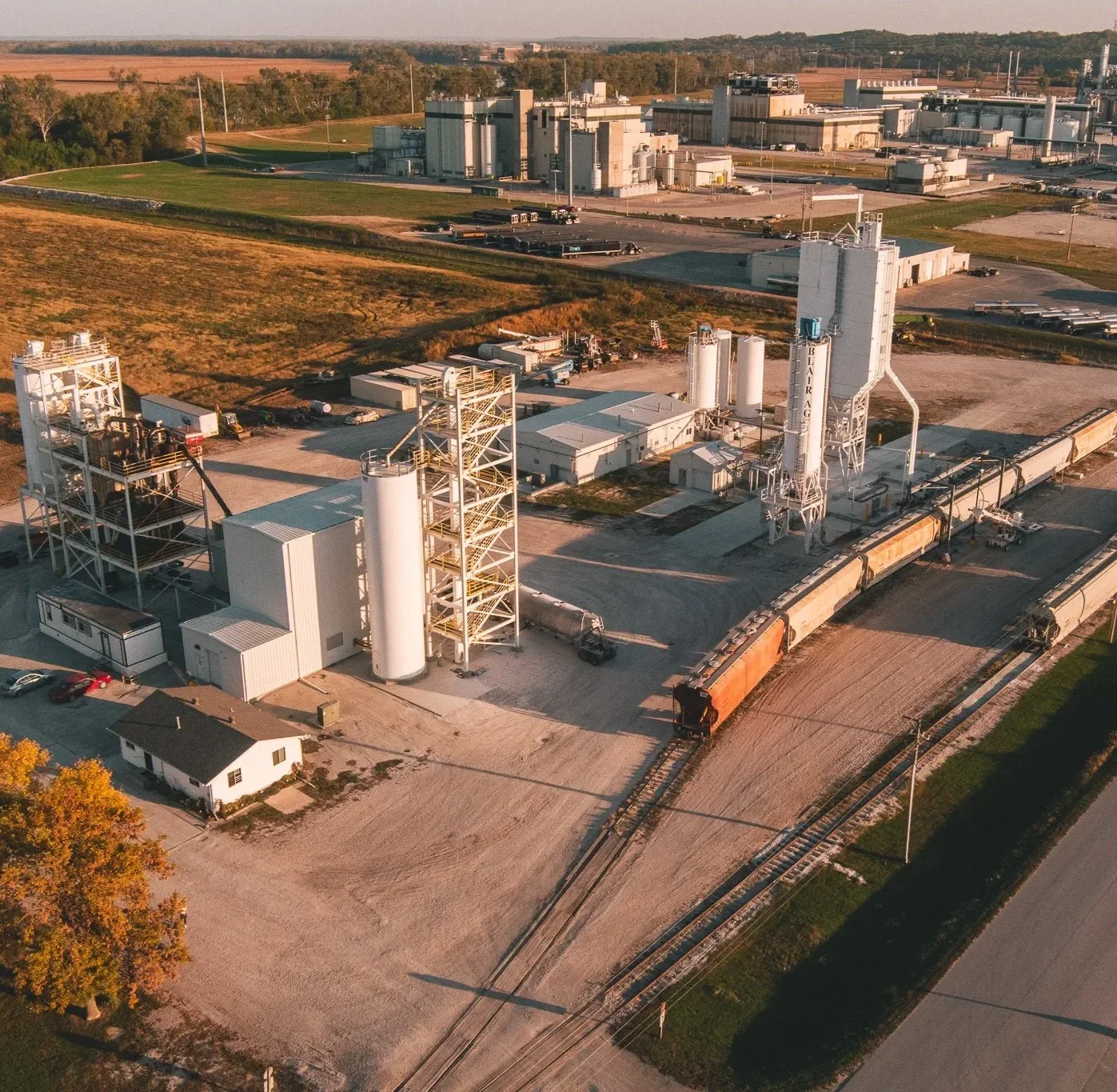 Aerial view of a cement manufacturing plant with silos, industrial equipment, and train tracks.