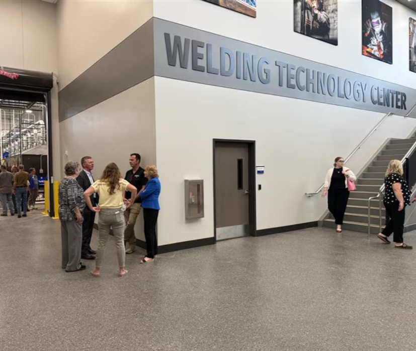 People standing and talking outside the Welding Technology Center in an industrial building, with some exiting via stairs and others near a garage door.