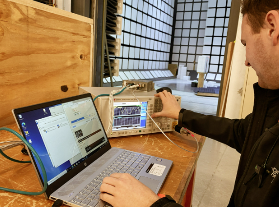 A person conducting electronic testing using a laptop and oscilloscope in a lab.
