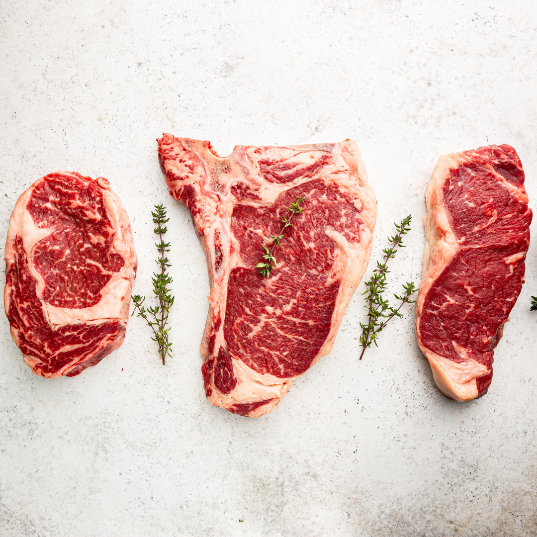 Three raw steaks with marbling, garnished with sprigs of thyme, on a white textured surface.