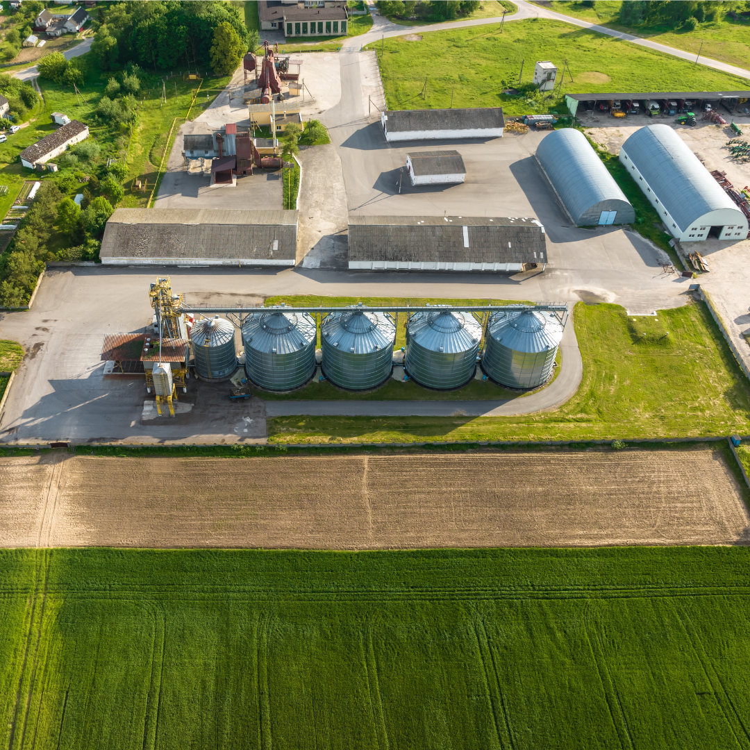 Aerial view of a farm with large silos, storage buildings, and green fields.