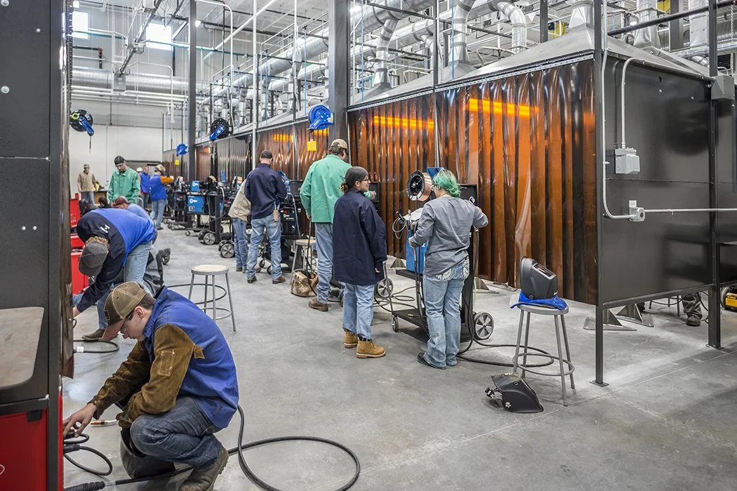 Group of people working with welding equipment inside a large industrial workshop.
