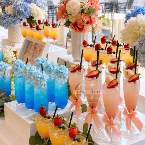 Colorful assortment of summer-themed drinks with fresh fruit garnishes on a floral table display.