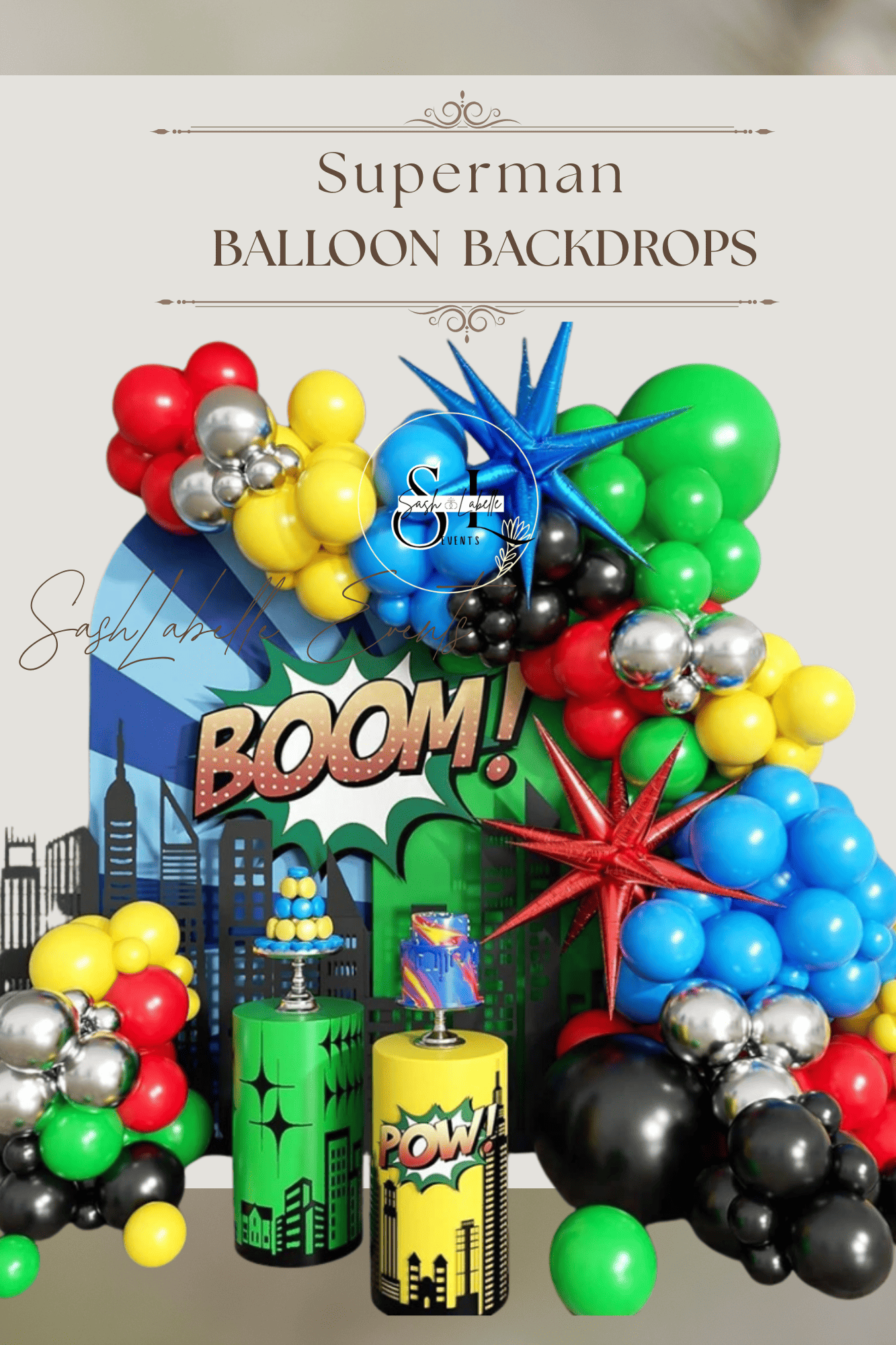 Superman themed balloon backdrop with cityscape, comic book style 'BOOM!' and 'POW!' graphics, and colorful balloons in red, yellow, green, black, and blue arranged in clusters.