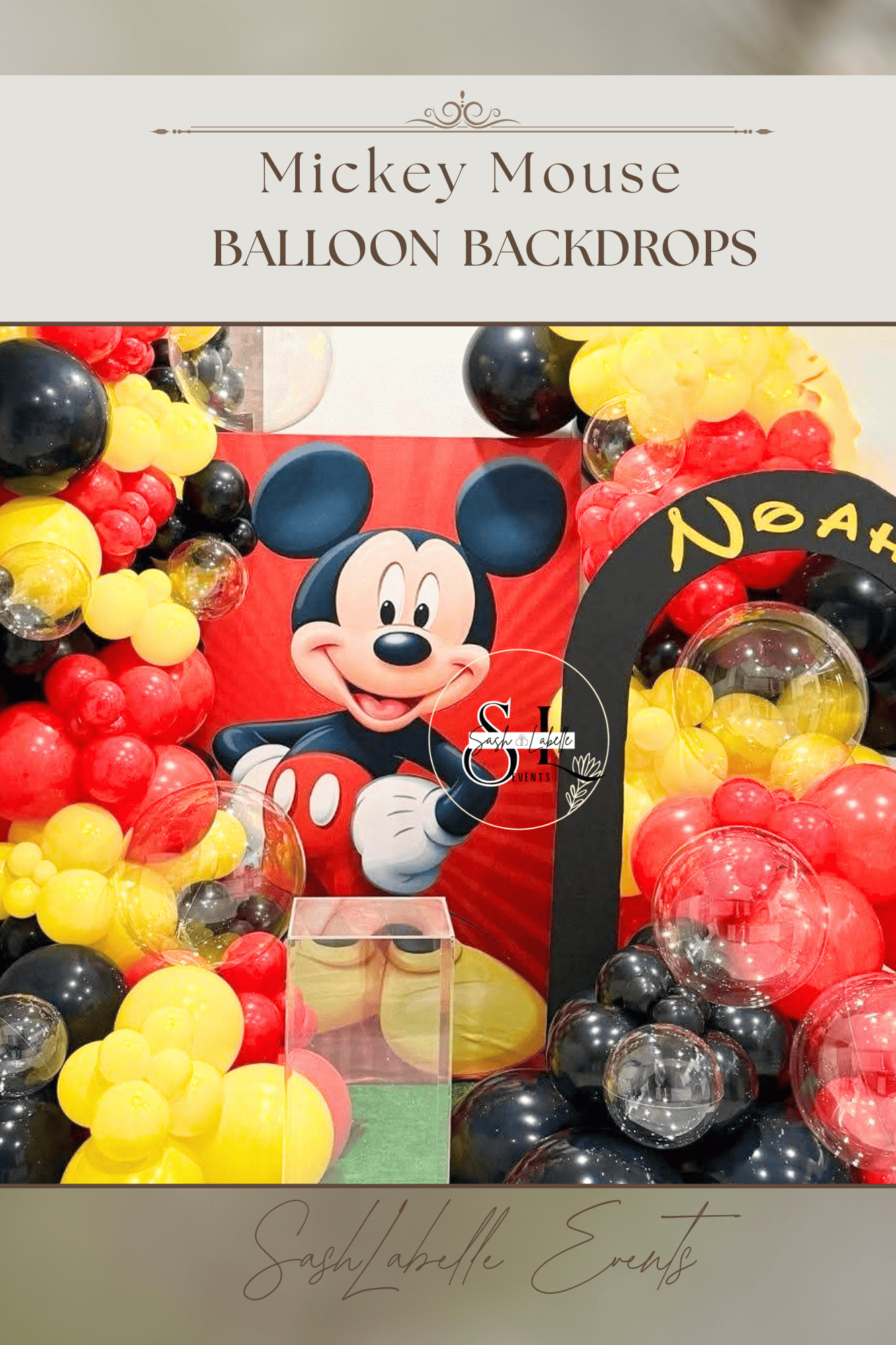 Decorative Mickey Mouse balloon backdrop with red, yellow, and black balloons, featuring a large Mickey Mouse face in the center and a sign that says 'Noah' in yellow letters.