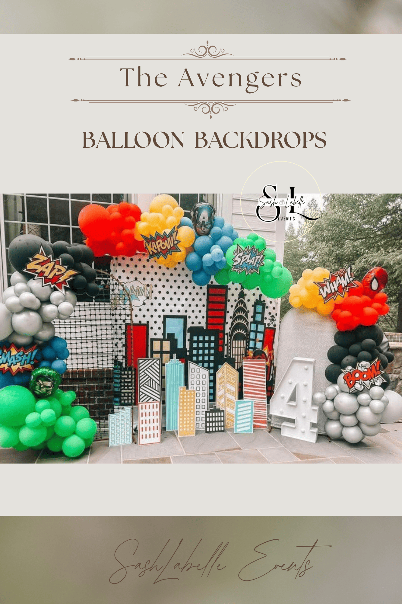 Decorative backdrop for a superhero themed event featuring city skyline cutouts, balloon arrangements in green, black, white, red, yellow, blue, and orange, comic book style speech bubbles with words like 'ZAP!', 'BANG!', 'WHAM!', 'SMASH!', and 'POW!