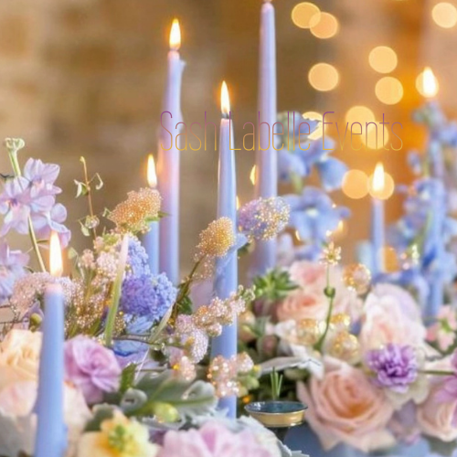 Elegant table centerpiece with lit candles, pastel flowers, and soft lighting for an event or celebration.