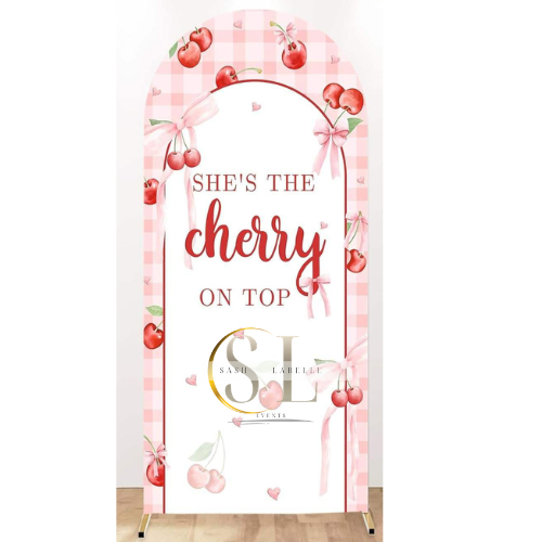 A decorative stand with a pink checkered border, hanging pink bows, and cherries, featuring the text "SHE'S THE cherry ON TOP" in red and gold lettering.