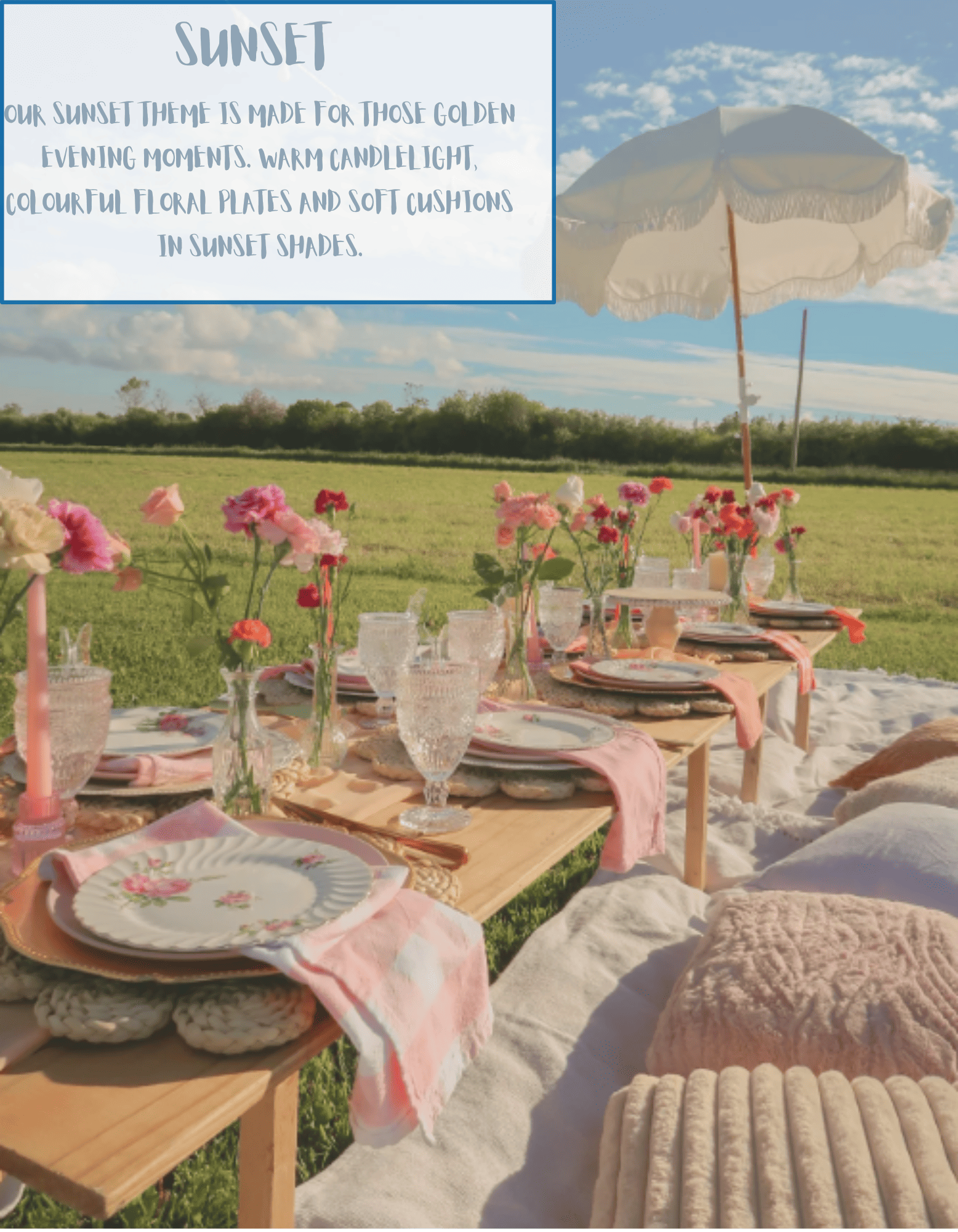 A table set for an outdoor sunset dinner with pink and white floral centerpieces, soft cushions, pink and white table linens, and elegant dinnerware, overlooking a grassy field with a blue sky and scattered clouds.
