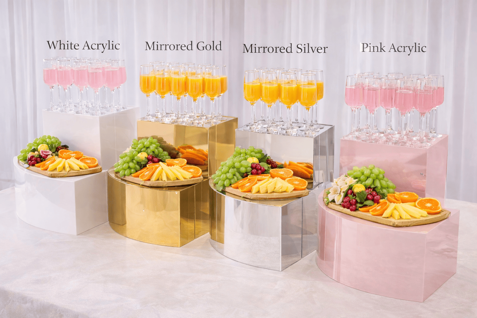 Display of four different types of champagne in tall glasses, labeled from left to right as White Acrylic, Mirrored Gold, Mirrored Silver, and Pink Acrylic, with assorted fruit plates in front of each.