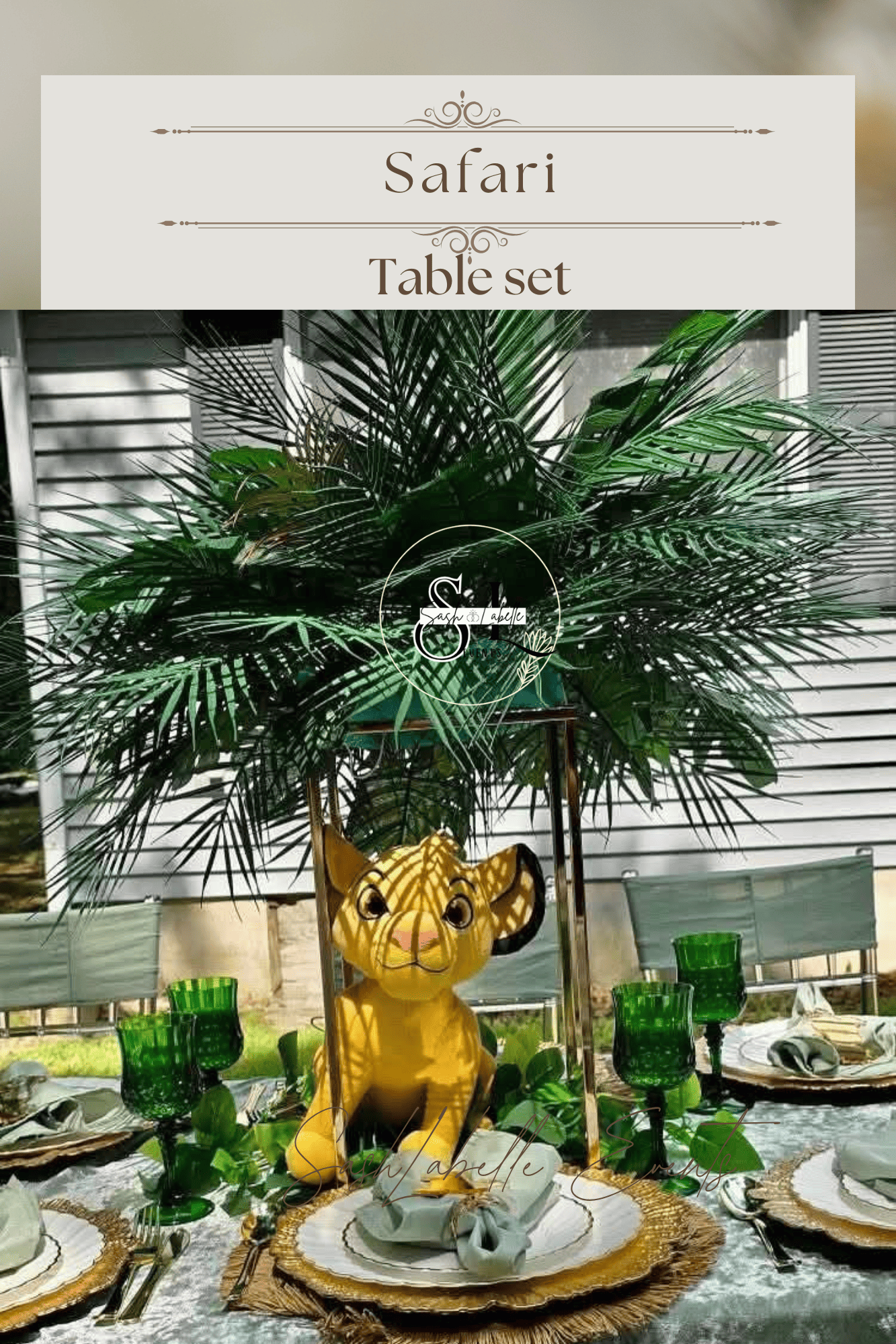 Table set for a safari-themed party with themed decorations, plates, utensils, glasses, and a lion mascot centerpiece decorated with greenery.