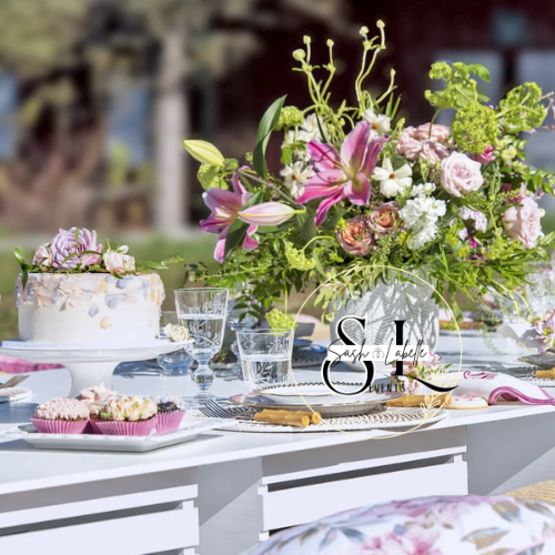Outdoor table setting with a large floral arrangement, desserts, clear glasses, and tableware.