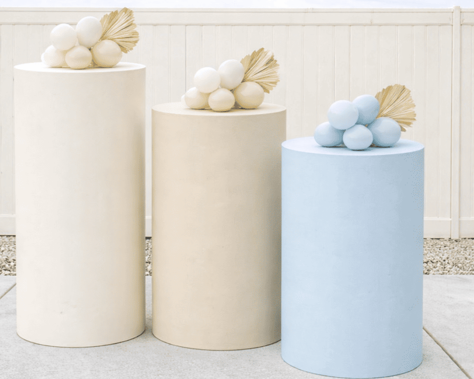 Three cylindrical pedestals with rounded tops, each decorated with a cluster of spherical objects and a gold-colored leaf, against a white wall.