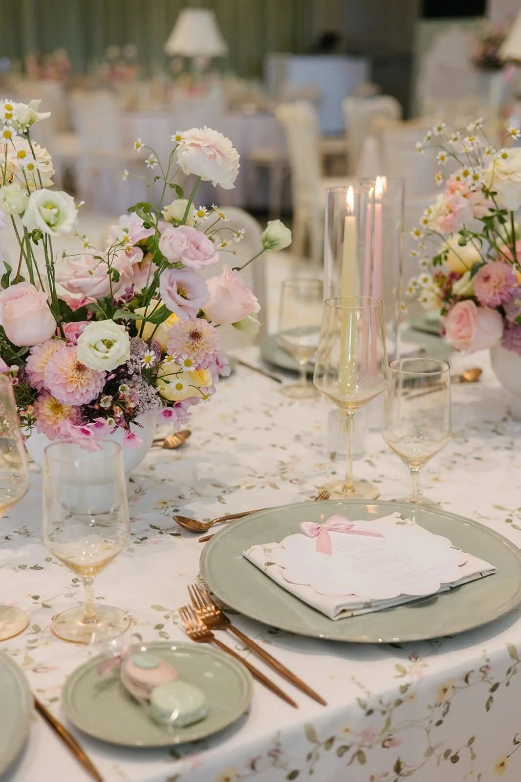 Elegant wedding reception table setting with pink and white flowers, gold cutlery, champagne glasses, and a floral tablecloth.