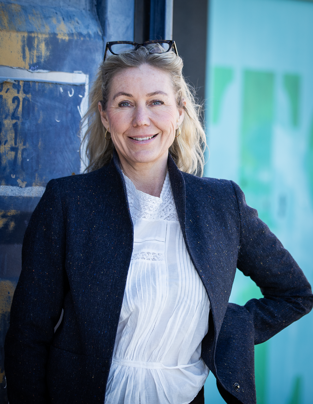 Karen Schou, iført en mørk blazer og hvid bluse, står foran en væg med graffiti.
