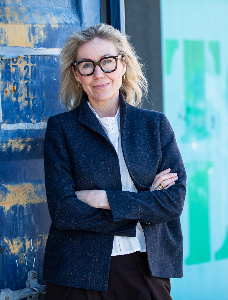 Karen Schou, der står udenfor med armene krydset, iført en mørk blazer, baggrund med graffititapet og væg.