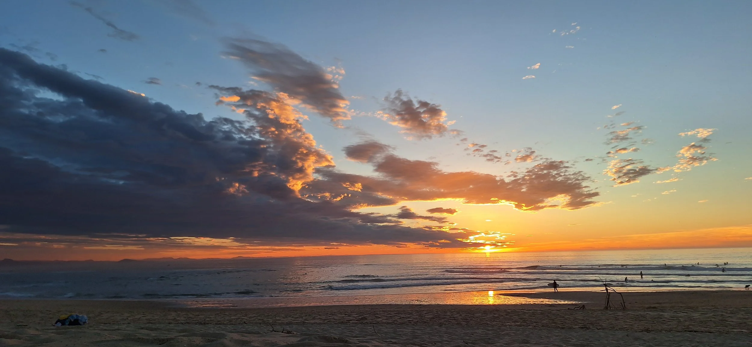 Coucher de soleil sur la mer avec nuages colorés dans le ciel, des silhouettes de personnes sur la plage.