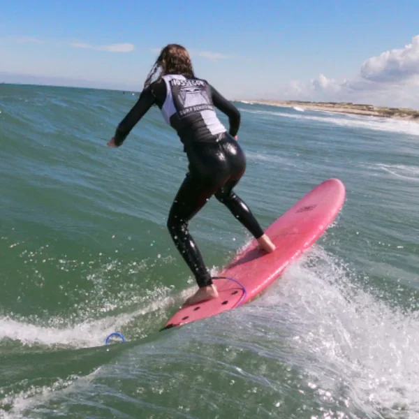 Personne faisant du surf sur une vague à la plage, vue de derrière, avec un ciel partiellement nuageux.