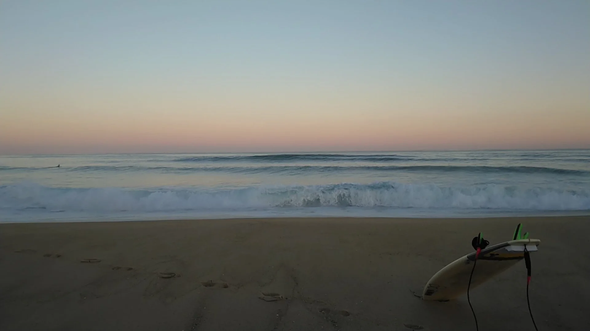 Plage au coucher du soleil avec deux planches de surf et une paire de palmes sur le sable.