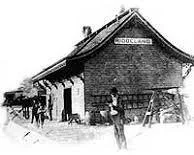A black-and-white photo of a historic train station building labeled 'COAL PLANT' with people and train cars nearby.