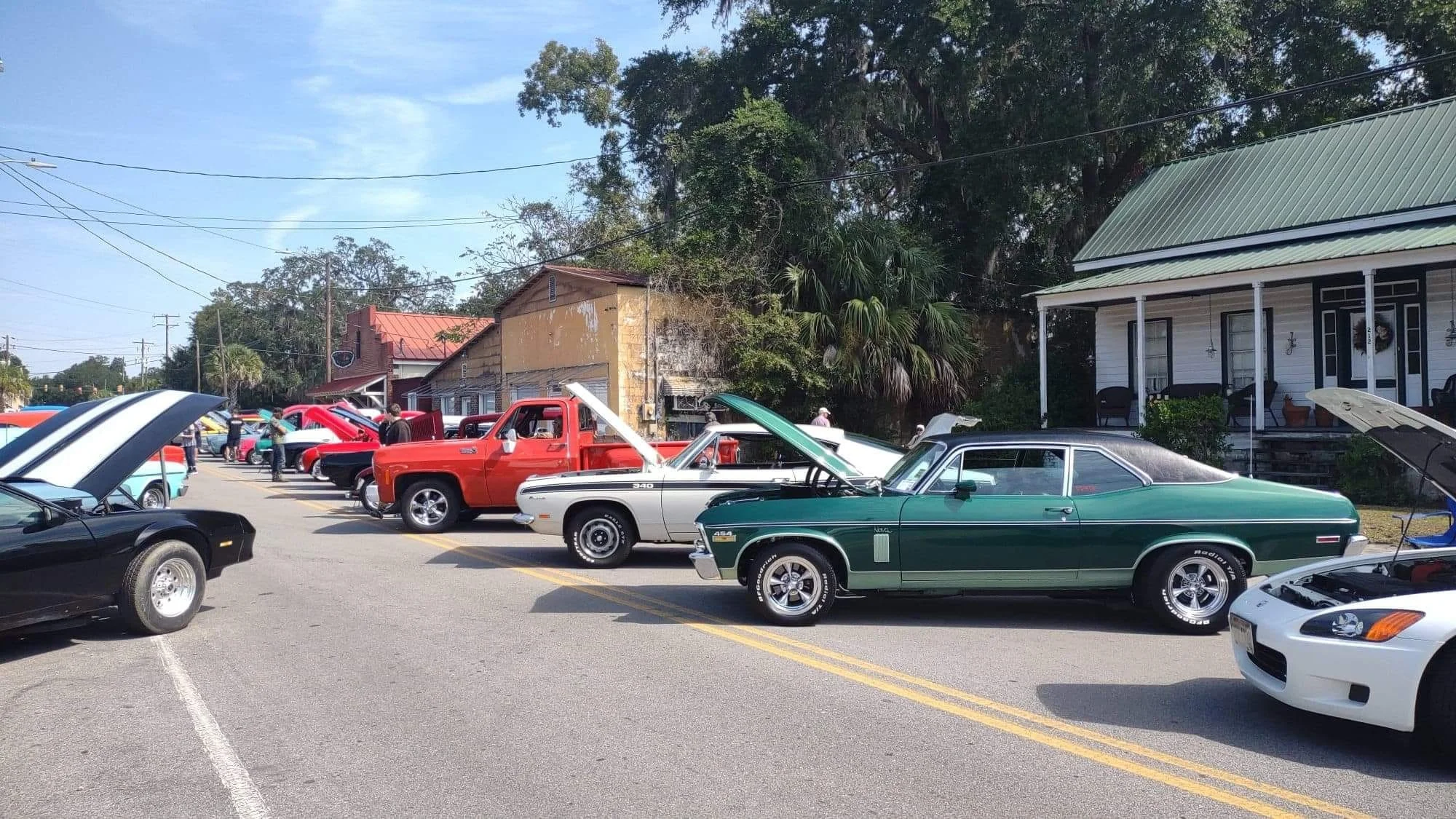 A classic car show with photos of vintage cars parked in a lot, some with hoods open, and a house with porch in the background.