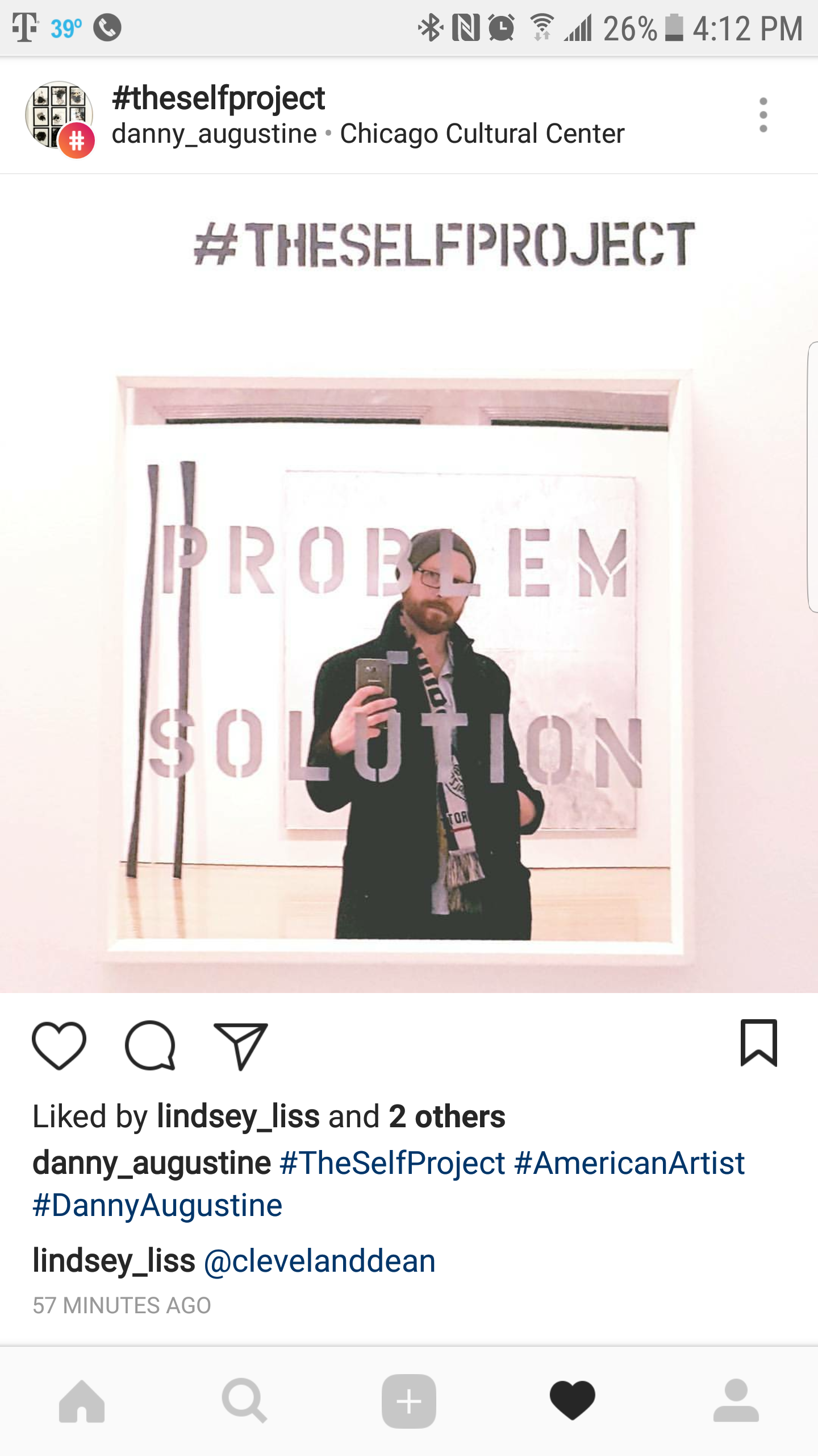 A man taking a mirror selfie at the Chicago Cultural Center, standing behind a glass with the words 'PROBLEM SOLUTION' and the hashtag '#THESelfPROJECT' displayed on the wall.
