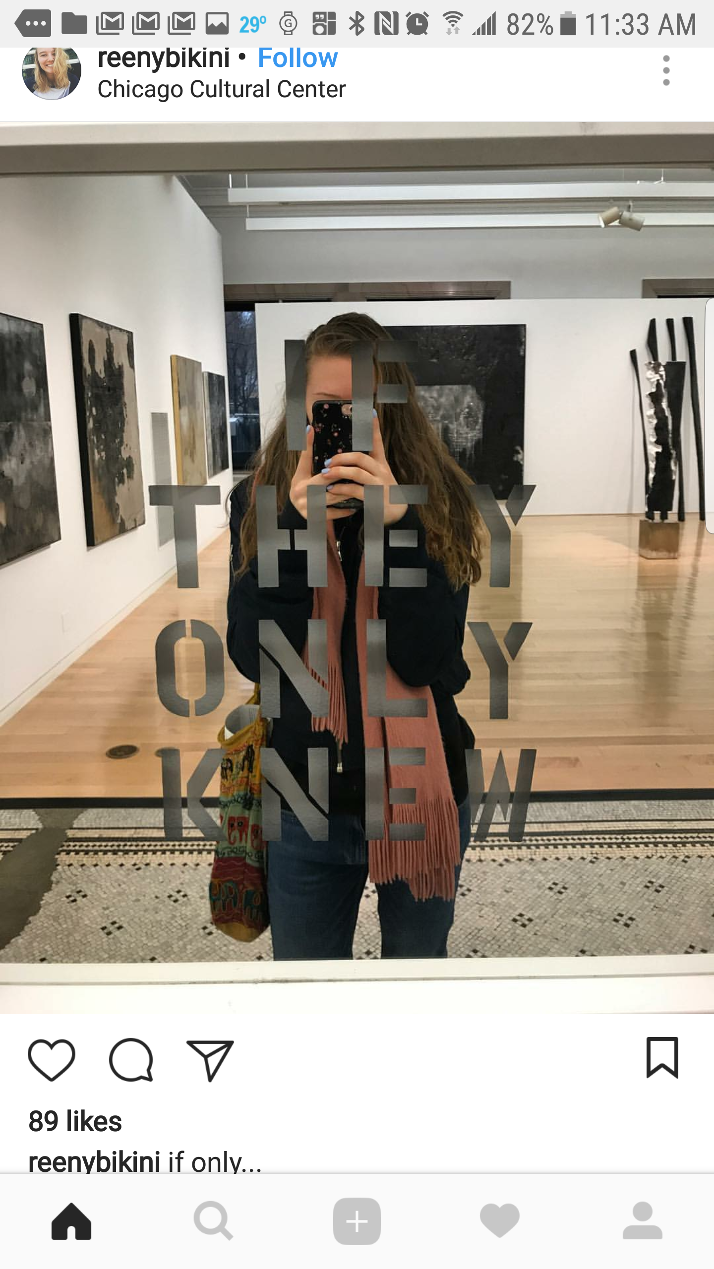 A person taking a mirror selfie at the Chicago Cultural Center. They are wearing a dark jacket, pink scarf, and carrying a colorful bag. The mirror has the words "THE ONLY KEY NOW" written on it. The background features artworks on the white walls an