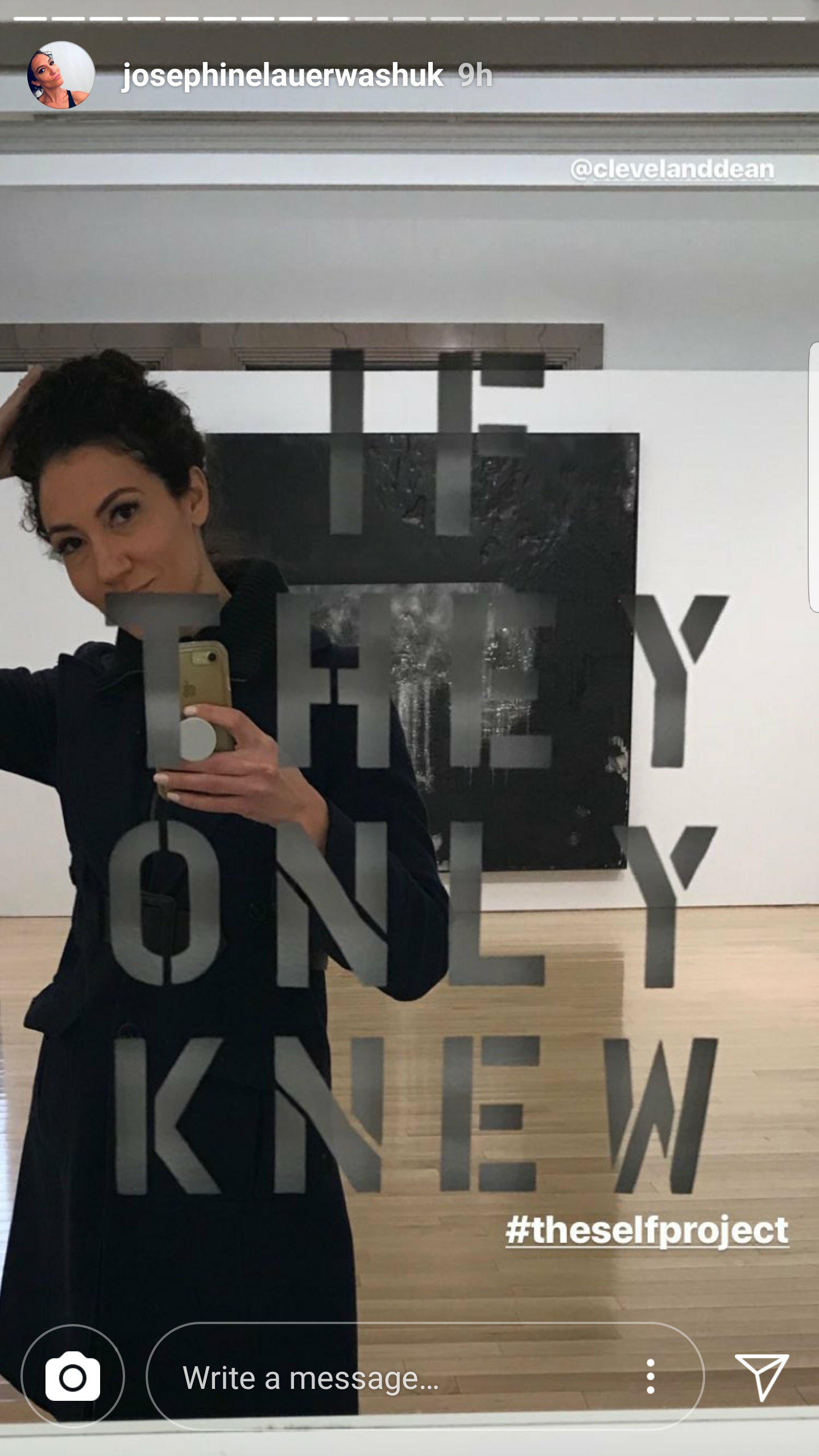 A woman taking a mirror selfie in an art gallery with a black and white landscape painting in the background. The mirror has the words 'THE ONLY WAY IS NEW' written on it, and there is a hashtag '#theselfproject' at the bottom.