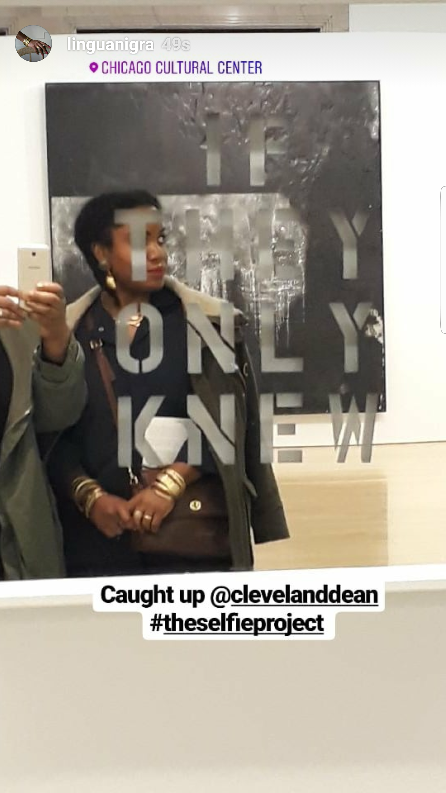 Woman standing in front of a mirror at the Chicago Cultural Center, taking a selfie with her smartphone, wearing jewelry and a coat.