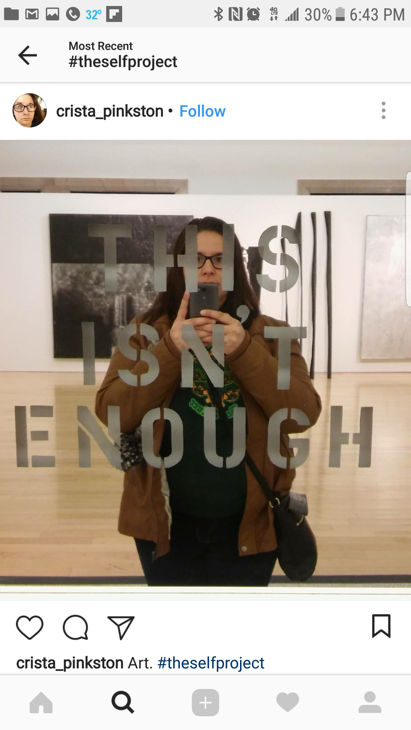 A woman taking a selfie in a mirror in an art gallery, with the quote "The art is enough" reflected behind her.