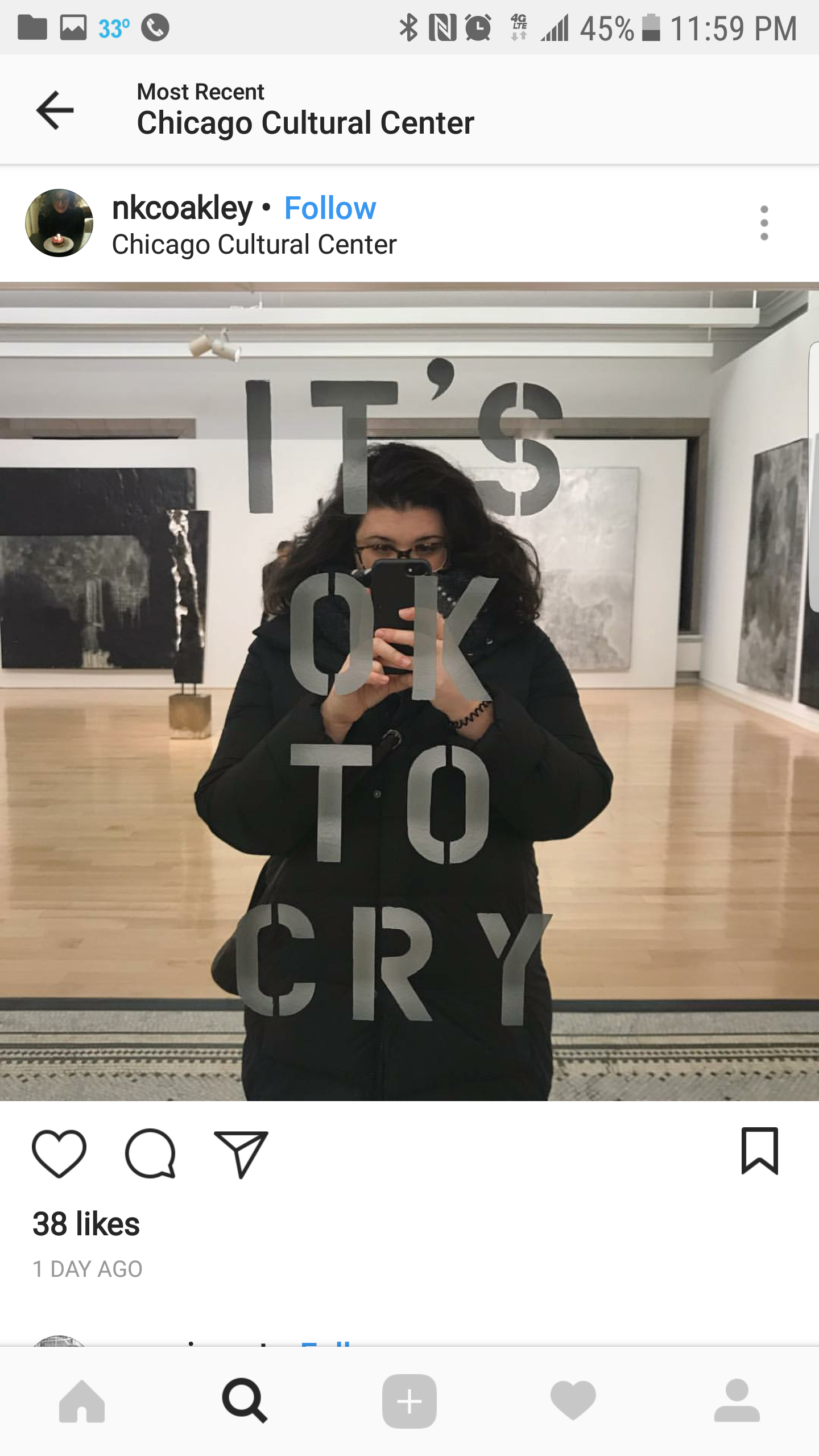 A woman taking a mirror selfie at an art gallery, with the words "IT'S OK TO CRY" written on the mirror.